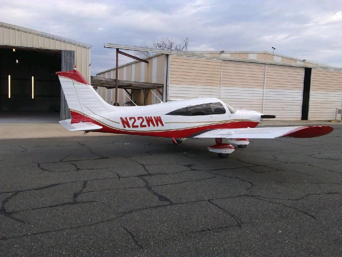 Single-engine Piper in a red and white scheme, three-quarter rear view